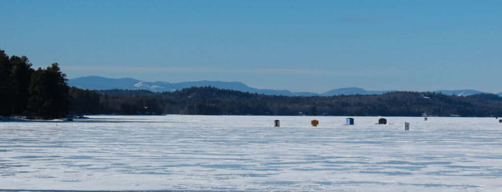 Image of various structures on Long Lake where people are ice fishing. A sturdy foundation of lake ice is necessary for this activity